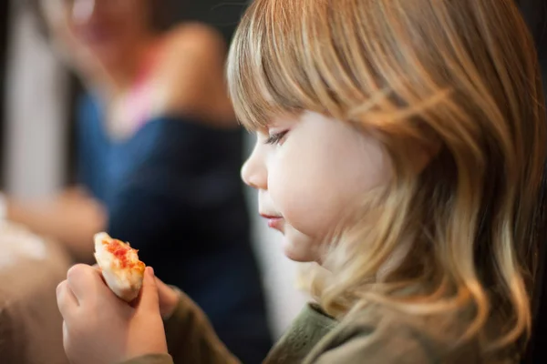 Pieni lapsi etsii pizza reuna ennen syödä sitä — kuvapankkivalokuva