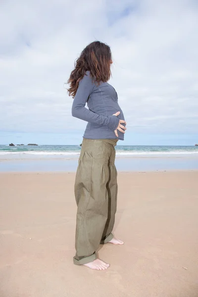 Gravid på stranden händer på magen — Stockfoto
