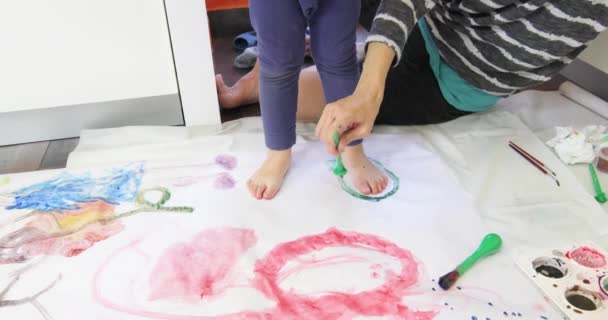 Женщина очерчивает ноги ребенка зеленым акварелью — стоковое видео