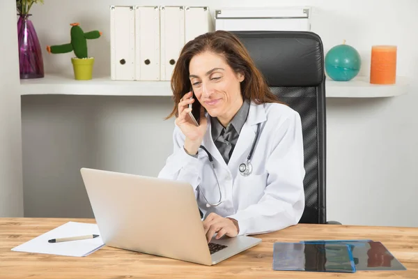 Doctor woman talking on phone and typing laptop — Stock Photo, Image