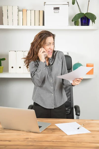Разъяренная деловая женщина кричит на мобильный телефон с документом в руке — стоковое фото