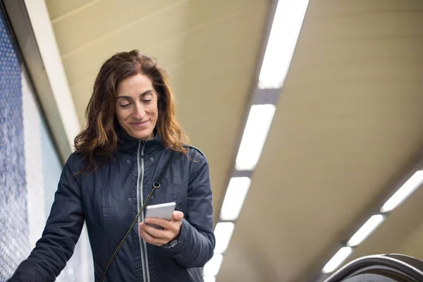 Улыбающаяся женщина в проходе метро читает мобильный телефон — стоковое фото