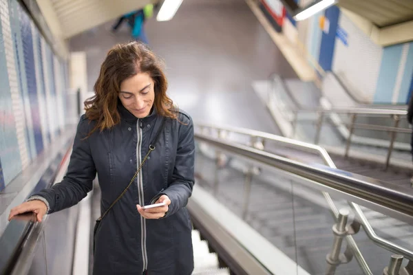 Mulher no metrô mecânico escadas lendo telefone — Fotografia de Stock