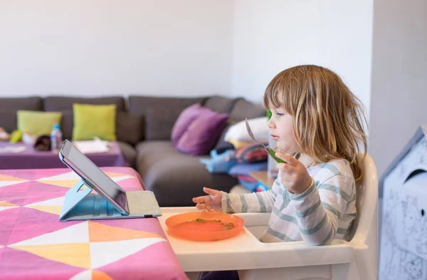 Kleines Kind im Hochstuhl isst vor digitalem Tablet — Stockfoto