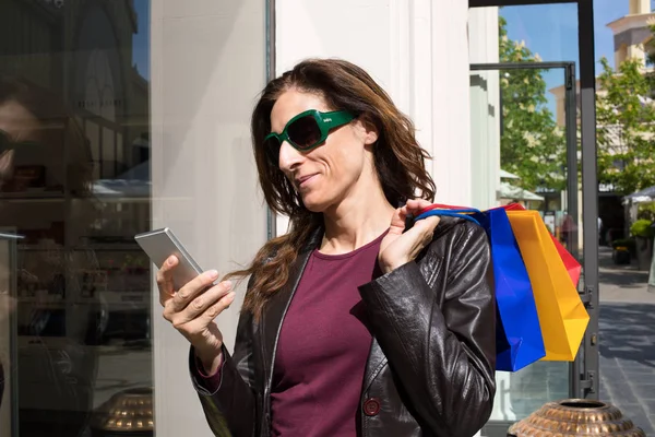 Mujer al lado de escaparate tienda usando el teléfono móvil —  Fotos de Stock