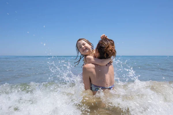 Kind en moeder spelen met golven in strand — Stockfoto