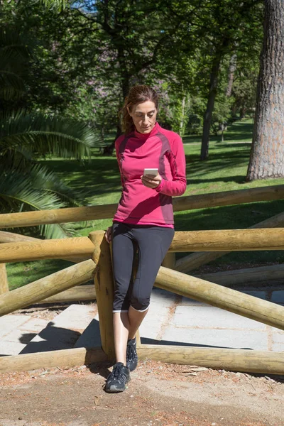 Sportovní žena v dřevěných zábradlí pomocí mobilní — Stock fotografie