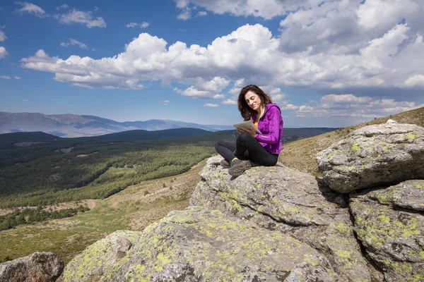 Женщина, сидящая на вершине горы, печатая на планшете — стоковое фото