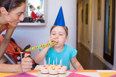 Anne ve pasta yanındaki parti üfleyici üfleyen çocuk