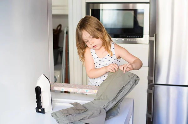 Little girl ironing and trousers in kitchen — Stock Photo, Image