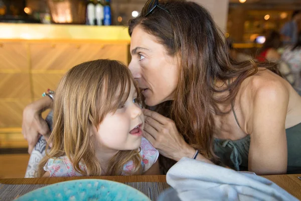 Mutter erzählt Mädchen im Restaurant ein Geheimnis ins Ohr — Stockfoto