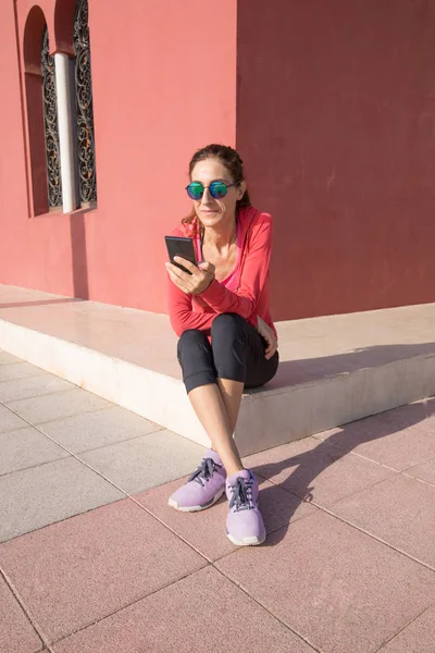 Kobieta za pomocą telefonów komórkowych, siedzi w rogu budynku — Zdjęcie stockowe