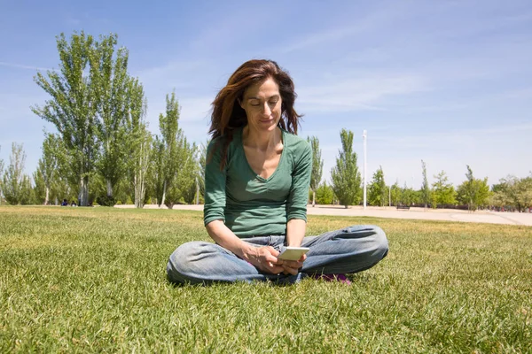 Vrouw met behulp van de mobiele telefoon zitten in park — Stockfoto