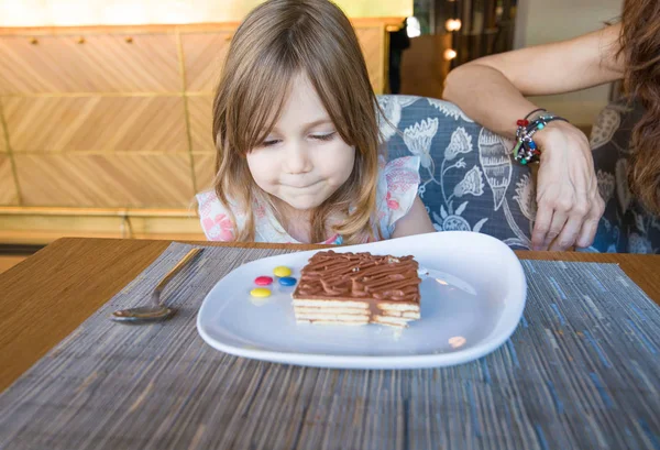 Маленькая девочка смотрит часть шоколадного торта в ресторане — стоковое фото