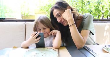 küçük çocuk ve anne restoranda mobil izlerken
