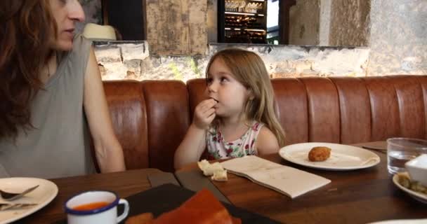 Little child eating olive talking to mother in restaurant — Stock Video