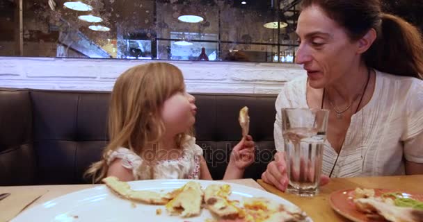 Klein meisje en moeder in restaurant lachen en eten van pizza — Stockvideo