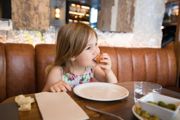 Kleines Mädchen isst Kroketten mit der Hand im Restaurant — Stockfoto