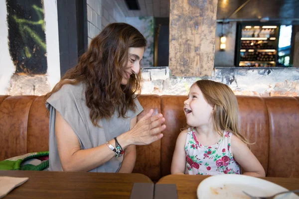 Menina rindo com a mãe sentada no restaurante — Fotografia de Stock