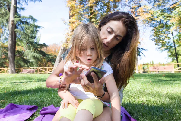 Žena a malá holčička s překvapením tváří, sledování mobilní sedí — Stock fotografie