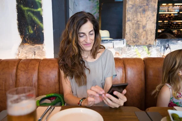 Mujer viendo móvil en restaurante sentado al lado de niña — Foto de Stock
