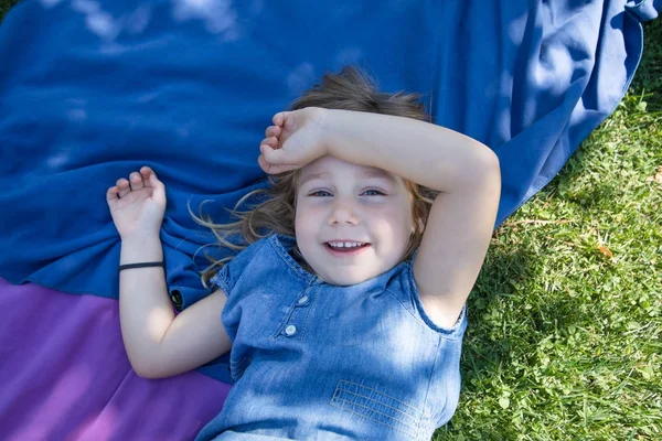 Flicka liggande i parken tittar och ler med arm i huvud — Stockfoto