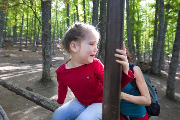 Little girl sitting on a fence in forest screaming to mother — Stock Photo, Image