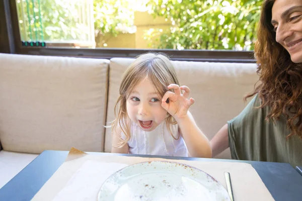 Funny girl teasing next to mother sitting in restaurant — Stock Photo, Image