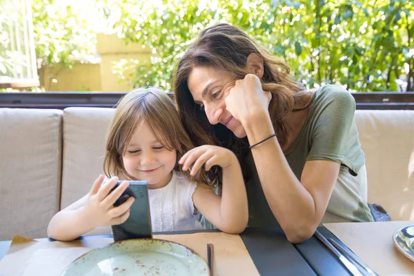 Pieni lapsi ja äiti katsomassa älypuhelinta ravintolassa — kuvapankkivalokuva