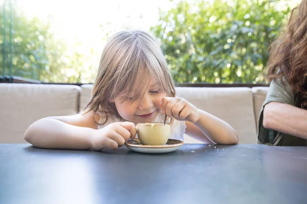 Criança sorrindo e brincando com xícara de café e colher — Fotografia de Stock