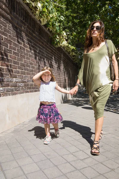 Küçük kız ve annesi el içinde el sokakta yürüme. — Stok fotoğraf