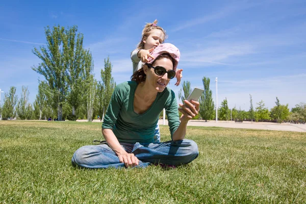 Criança brincando com mãe lendo telefone no parque — Fotografia de Stock