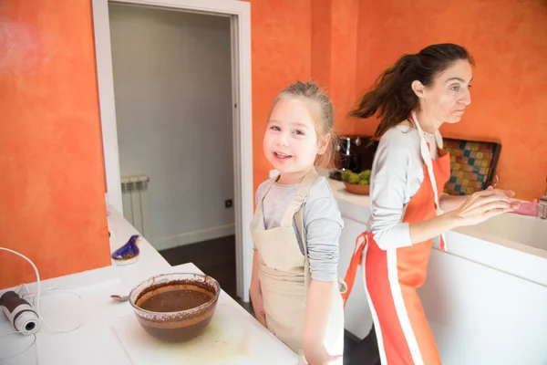 Kleines Mädchen schaut zu und Mutter kocht Kuchen in der Küche — Stockfoto