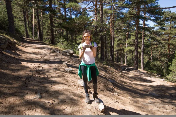 Frau beobachtet Handy, um zwischen zwei Wegen im Wald wählen zu können — Stockfoto
