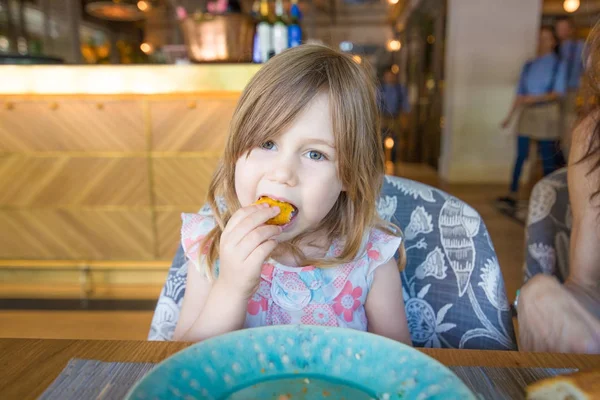 Menina olhando e comendo croquete com a mão no restaurante — Fotografia de Stock