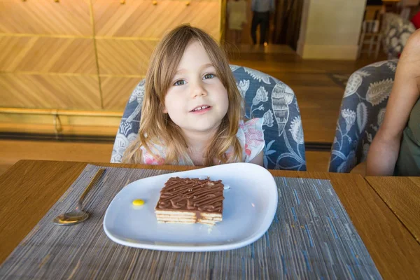 Kleines Mädchen sucht mit Portion Schokoladenkuchen im Restaurant — Stockfoto