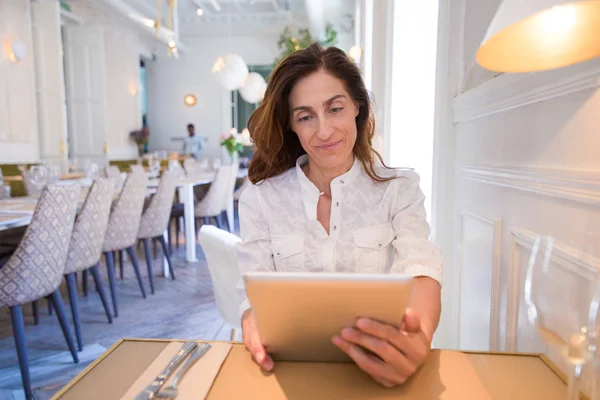 Mujer en restaurante leyendo tableta — Foto de Stock