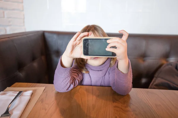 Μικρό παιδί στο εστιατόριο προβολή κενή οθόνη του κινητού τηλεφώνου — Φωτογραφία Αρχείου