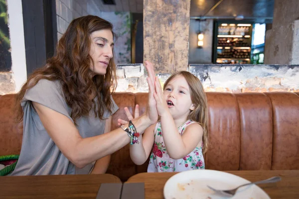 Little girl and mother in restaurant playing with hands — Stock Photo, Image