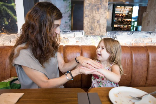 Feliz chica y madre en restaurante jugando con las manos Fotos de stock