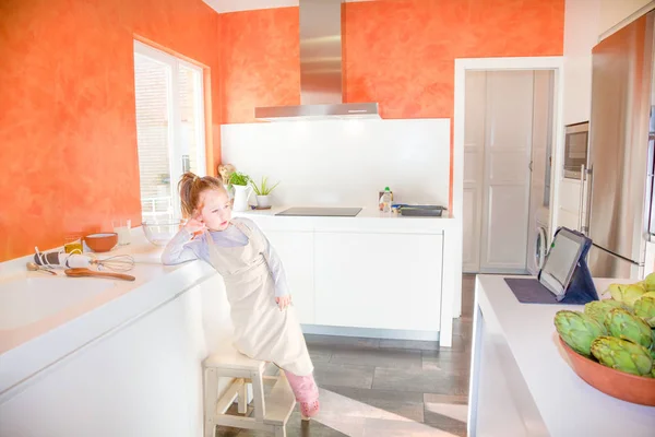 Kleine Kinderköchin schaut in der Küche auf Tablet — Stockfoto