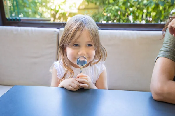 Little girl with spoon in hands smiling in restaurant — Stock Photo, Image