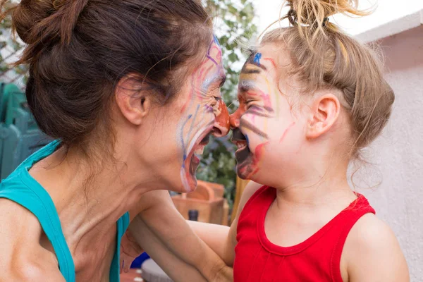 Lächelndes kleines Mädchen und Mutter mit aufgemaltem Gesicht schauen genau hin — Stockfoto