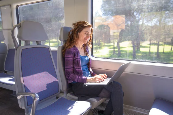 Mujer sonriente en tren escribiendo en el ordenador portátil Fotos de stock libres de derechos