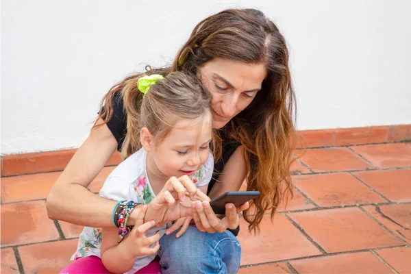 Женщина печатает на мобильном телефоне и маленькая девочка смотрит улыбаясь — стоковое фото