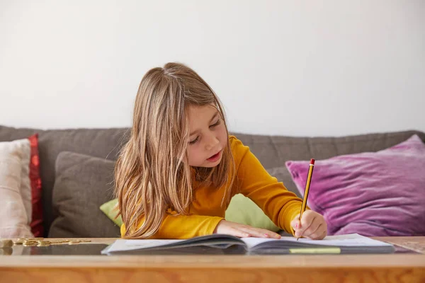 Sechsjähriges Mädchen Sitzt Hause Auf Braunem Sofa Und Schreibt Schulheft Stockbild