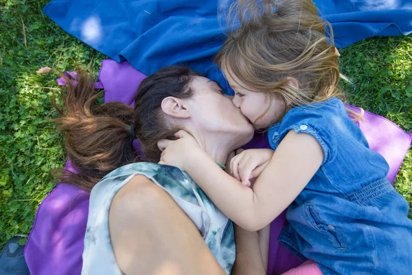 Little girl kissing to mother lying on the ground — ストック写真