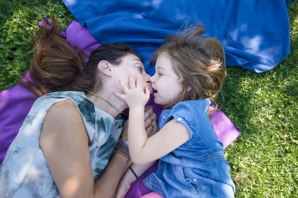 Little girl and mother kissing lying in the park — Stok fotoğraf