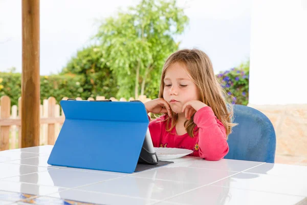 Kleines Mädchen sitzt vor digitalem Tablet mit ernstem Ausdruck — Stockfoto