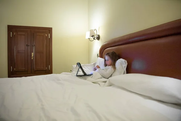 Маленька дівчинка лежить на ліжку дивиться планшет вночі — стокове фото